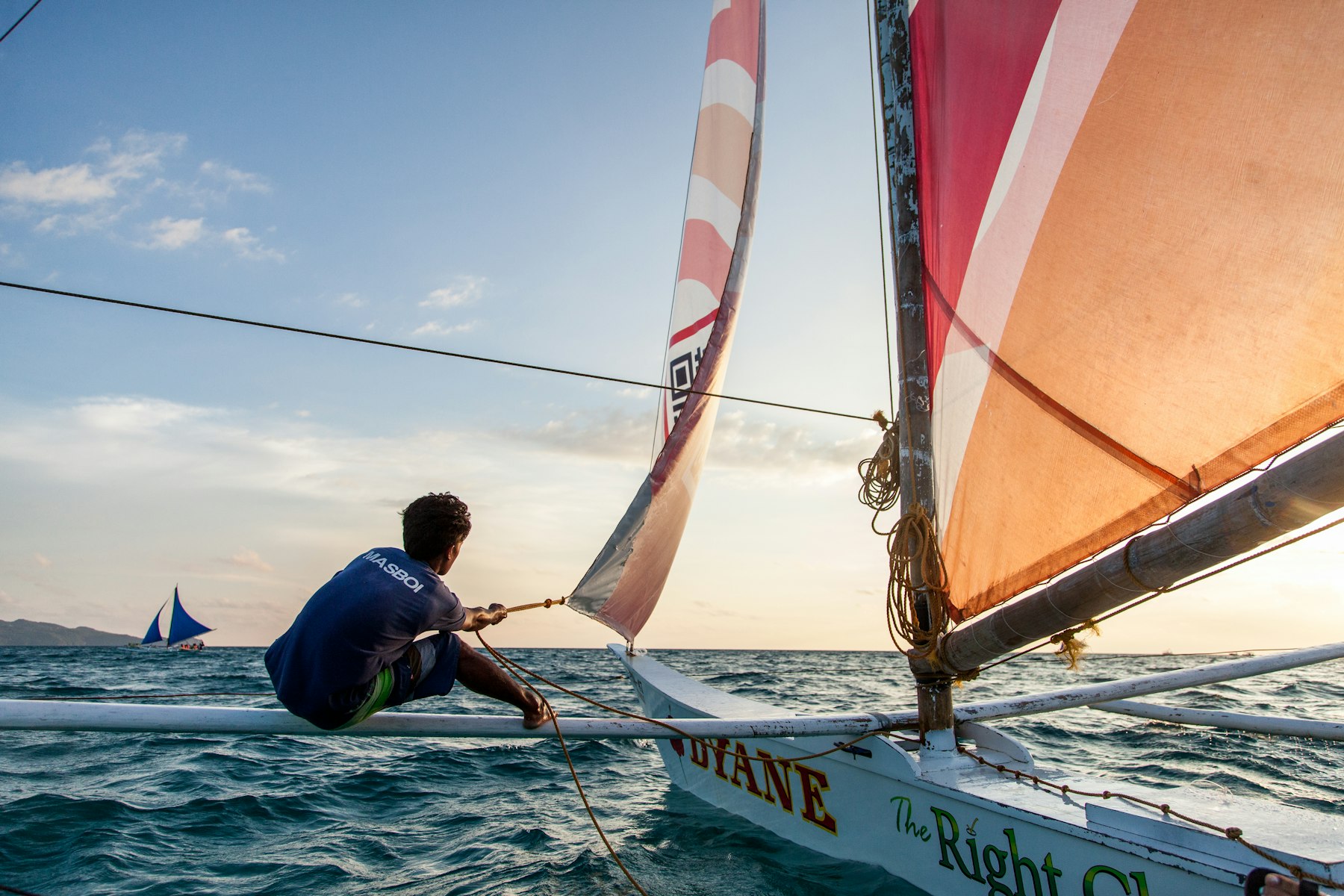 Velejador ajustando a vela ao entardecer
